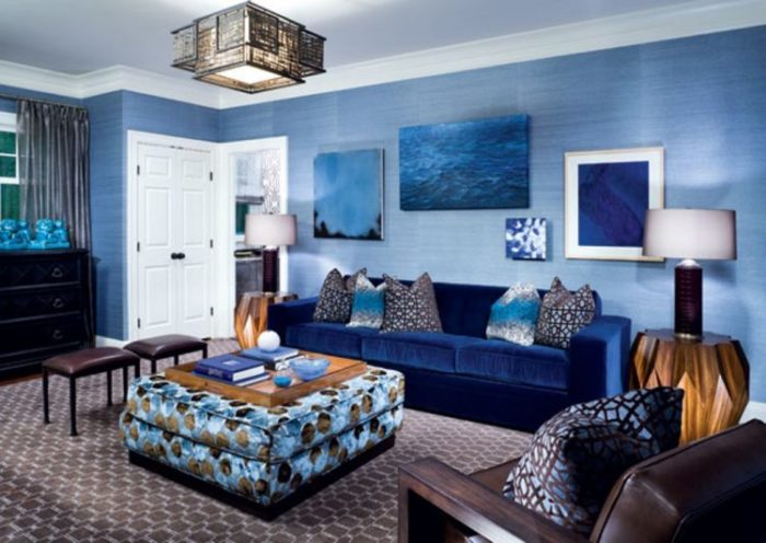 غرفة معيشة تتكون من كنبة كبيرة زرقاء بخامة القطيفة مع كرسي من الجلد باللون البني